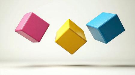Three solid wooden cubes, painted in vibrant pink, yellow, and blue, are suspended in mid-air against a soft, gradient white background. The simple composition and bright colors create a playful and abstract image. This could represent concepts of primary colors, building blocks, or children's toys.の素材