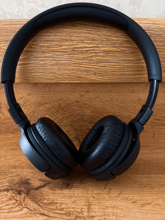 Stylish black wireless headphones lie on a wooden shelf. Using headphones to listen to music or to...