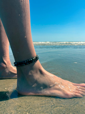 Beautiful female legs with a bracelet on the beach. Sea wave washes female legs