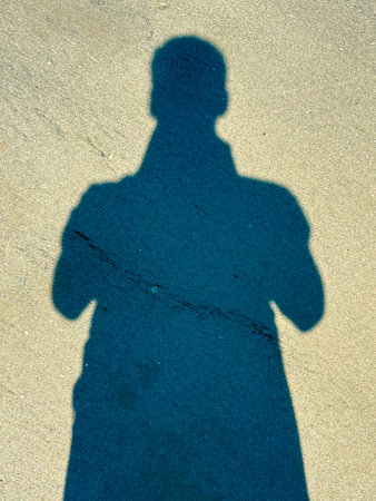 The shadow of a man standing on the sand on a clear sunny day. Sandy beachの写真素材