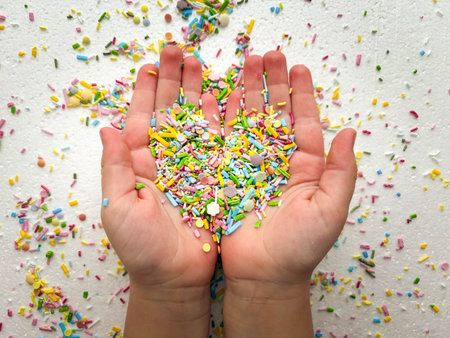 Sugar fine confectionery sprinkles form a heart shape in the palms of a child. Conceptual photo on a...