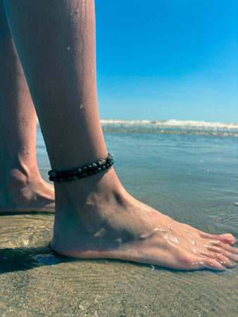 Beautiful female legs with a bracelet on the beach. Sea wave washes female legs