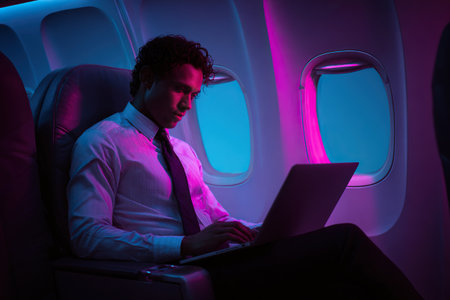 A successful businessman works on his laptop during a flight. Neon lighting in the airplane cabin. Business travel concept.の素材