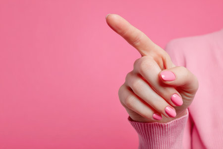 Woman with pink manicure pointing at something on pink background, close-up on her hand. Copy spaceの素材