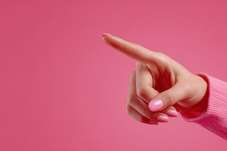 A woman's hand points at something on a pink background, close-up. Women's fingers with pink manicure.の素材