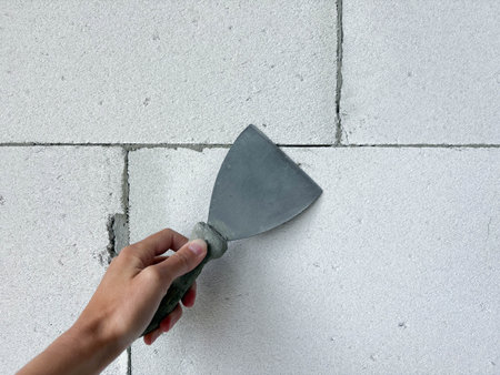 A hand with a spatula on a white block wall. Preparing for interior wall finishing. Home renovation and construction.の写真素材