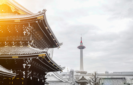 The famous heritage, traditional temple Hongan-ji with golden roof with Kyoto tower in dramatic bright morning sunrise light in Japanのeditorial素材