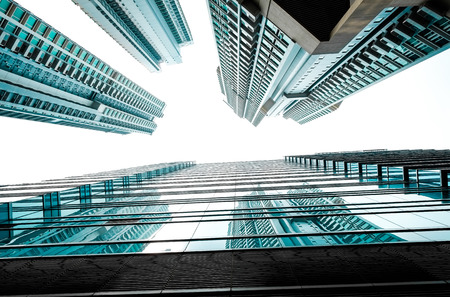 Business concept for real estate and corporate construction - looking up view in financial district, the silhouettes of skyscrapers city reflect blue sky, sun lightsの写真素材