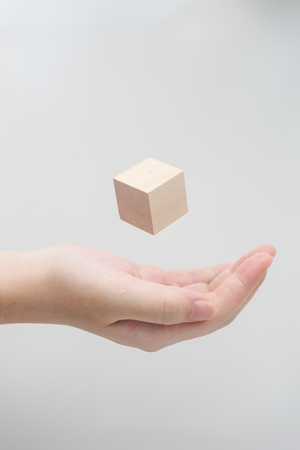 Surreal design concept - Abstract geometric real wooden cube float on girl's hand with grey background.の写真素材