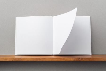 Design concept - front view of opened square white notebook on bookshelf and grey wall for mockupの写真素材