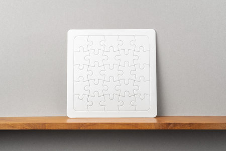 Design concept - front view of white square jigsaw puzzle on bookshelf and grey wall for mockup