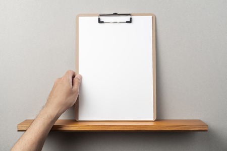 Design concept - man's hand hold A4 paper with clipboard on bookshelf and grey wall for mockupの写真素材