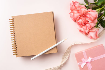 event design concept - top view of a bunch of pink rose , gift box , kraft notebook and vintage ribbon on pink background for mothers day and valentines day, wedding event with copy space for mock upの写真素材