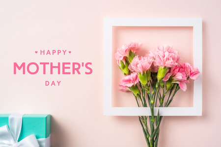event design concept - top view of a bunch of pink carnation with white photo frame, gift box and greeting word on pink background for mothers day event with copy space for mock upの写真素材