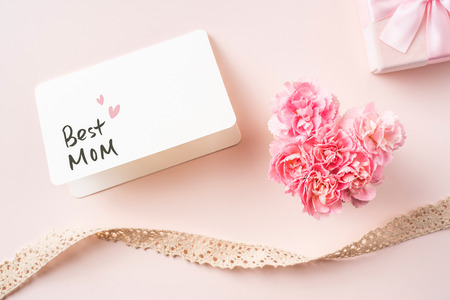 event design concept - top view of a bunch of pink carnation with white card, ribbon, gift box and greeting word on pink background for mothers day event with copy space for mock upの写真素材