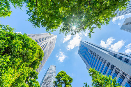 Asia Business concept for real estate, corporate construction and ecology - looking up view of panoramic modern city skyline with blue sky and green tree in shinjuku, tokyo, japanの写真素材