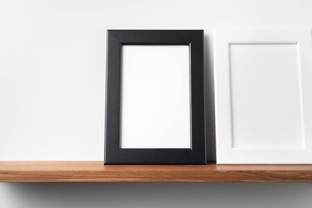Design concept - front view of vertical white and black wood photo frame on bookshelf and white wall for mockupの写真素材