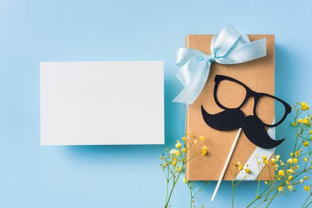 event design concept - top view of fathers day layout with ribbon kraft gift box, yellow flower and necktie on blue background, copy space for mock upの写真素材