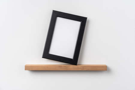 Design concept - front view of vertical black wood photo frame on bookshelf and white wall for mockupの写真素材