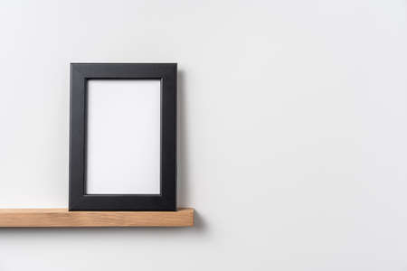 Design concept - front view of vertical black wood photo frame on bookshelf and white wall for mockupの写真素材
