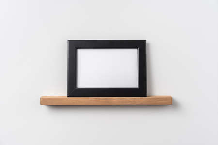 Design concept - front view of horizontal black wood photo frame on bookshelf and white wall for mockupの写真素材