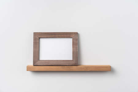 Design concept - front view of horizontal wood photo frame on bookshelf and white wall for mockupの写真素材