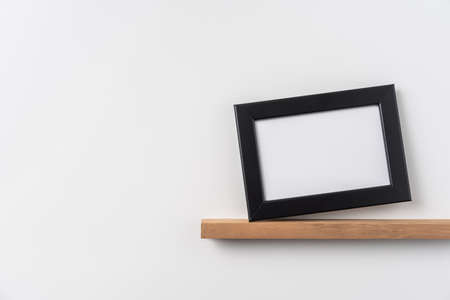 Design concept - front view of horizontal black wood photo frame on bookshelf and white wall for mockupの写真素材