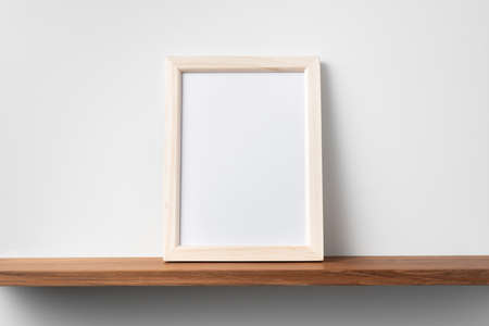 Design concept - front view of vertical wood photo frame on bookshelf and white wall for mockupの写真素材