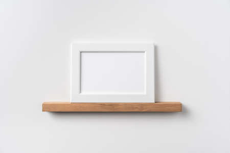 Design concept - front view of horizontal white wood photo frame on bookshelf and white wall for mockupの写真素材