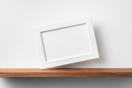 Design concept - front view of horizontal white wood photo frame on bookshelf and white wall for mockupの写真素材