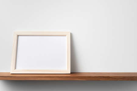 Design concept - front view of horizontal wood photo frame on bookshelf and white wall for mockupの写真素材