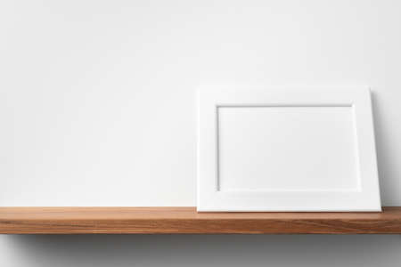 Design concept - front view of horizontal white wood photo frame on bookshelf and white wall for mockupの写真素材