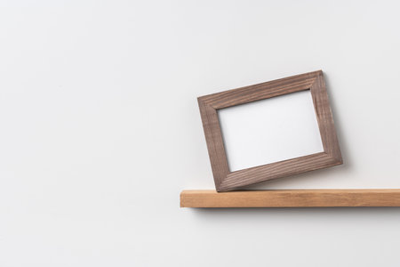 Design concept - front view of horizontal wood photo frame on bookshelf and white wall for mockupの写真素材