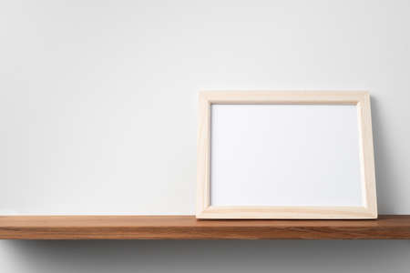 Design concept - front view of horizontal wood photo frame on bookshelf and white wall for mockupの写真素材