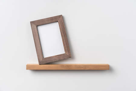 Design concept - front view of vertical wood photo frame on bookshelf and white wall for mockupの写真素材