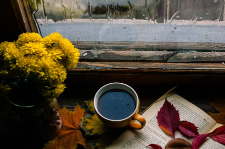 Autumn composition of a cup of coffee, a vase with chrysanthemums, colorful leaves and rainy window...