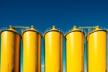 Row of yellow silos against blue sky with few clouds. Generative AI.の素材
