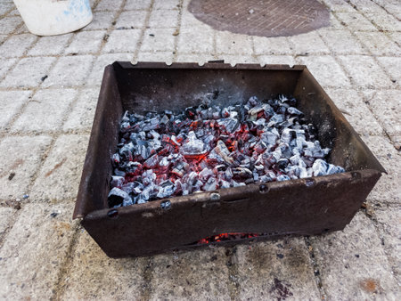 A metal box filled with lots of charcoal sitting on a sidewalk.の写真素材