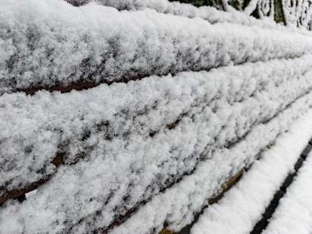 A wooden bench covered in snow next to a fence.の写真素材