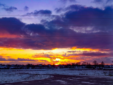 A sunset over a snowy field with power lines in the foreground.の写真素材