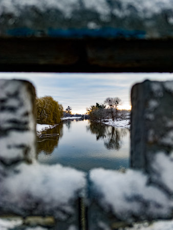 A view of a river through a window with snow on the ground.の写真素材