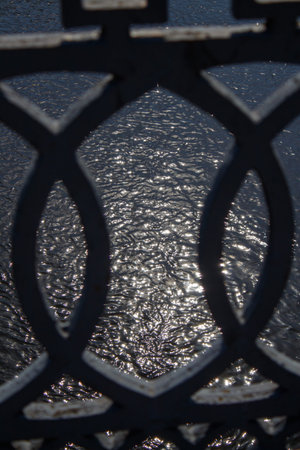A close up of a metal fence with water in the background.