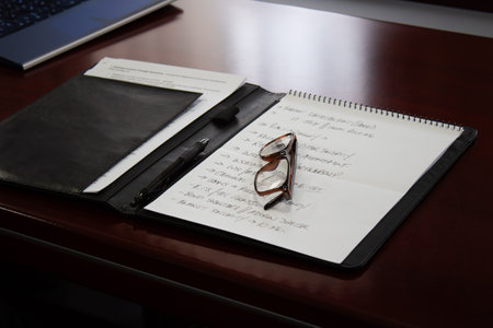 A notebook with a pen and glasses sitting on top of a desk.の写真素材