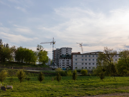 A large building with cranes in the background in a grassy field.の写真素材