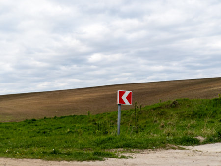 A red and white arrow sign sitting on the side of a dirt road.の写真素材