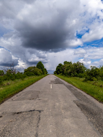 A long empty road in the middle of a grassy field under a cloudy sky.の写真素材
