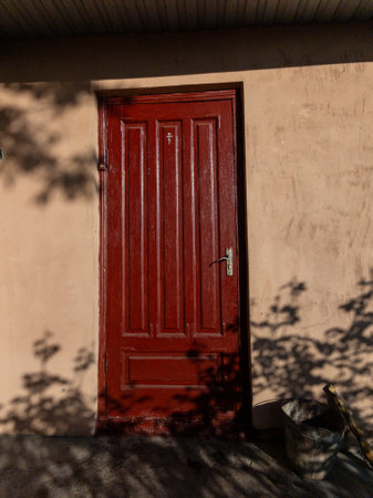 A red door on a beige wall with a bucket of water next to it.の写真素材