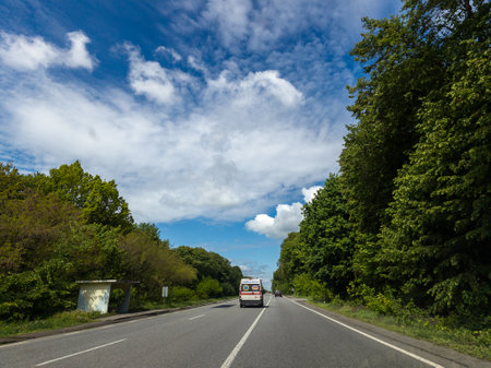 An ambulance is traveling on a road with trees on both sides.の写真素材