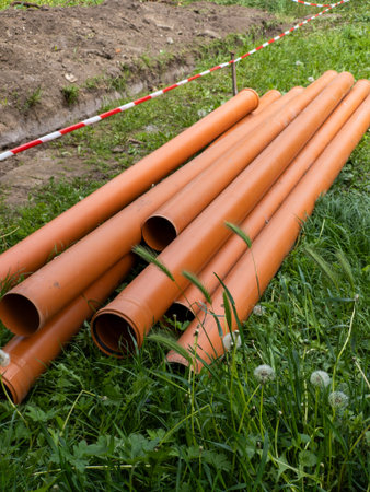 A bunch of orange pipes laying on the ground in the grass.
