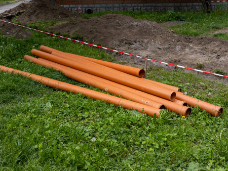 A bunch of orange pipes laying on the ground in the grass.